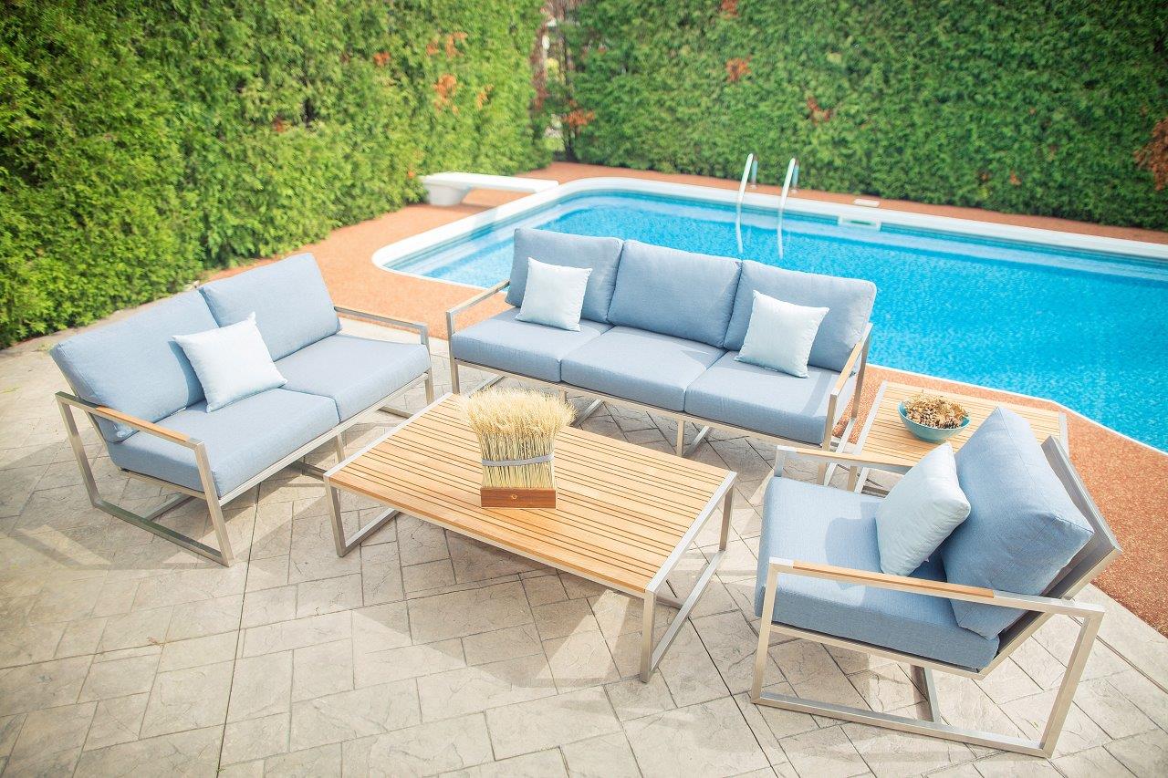 Acacia outdoor end table with stainless steel frame and teak top, surrounded by sofas in a new color by the pool in a modern setting.